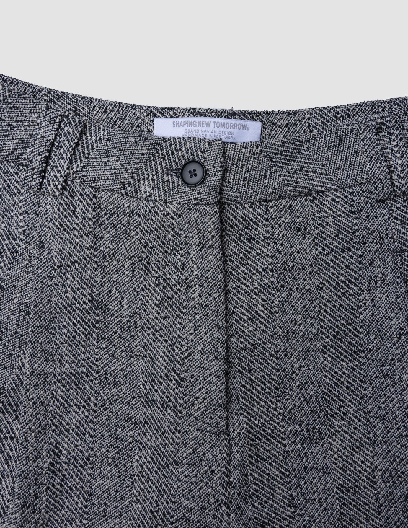 Nahaufnahme des Bunds der Damenhose Ashryn Pants Wide Domino Herringbone aus schwarz-weißem Bouclé mit einem einzelnen Knopf in der Mitte und einem weißen Markenetikett.